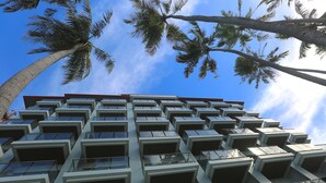 A modern hotel with a symmetrical facade, large windows, and a clear view of palm trees against a blue sky. - Kaani Grand Seaview (Maafushi)