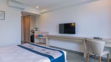 Habitació d'hotel amb llit, escriptori, cadira, televisió i petita cuina.