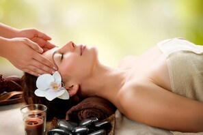 Una persona recibiendo un tratamiento facial con flores y piedras sobre una mesa.