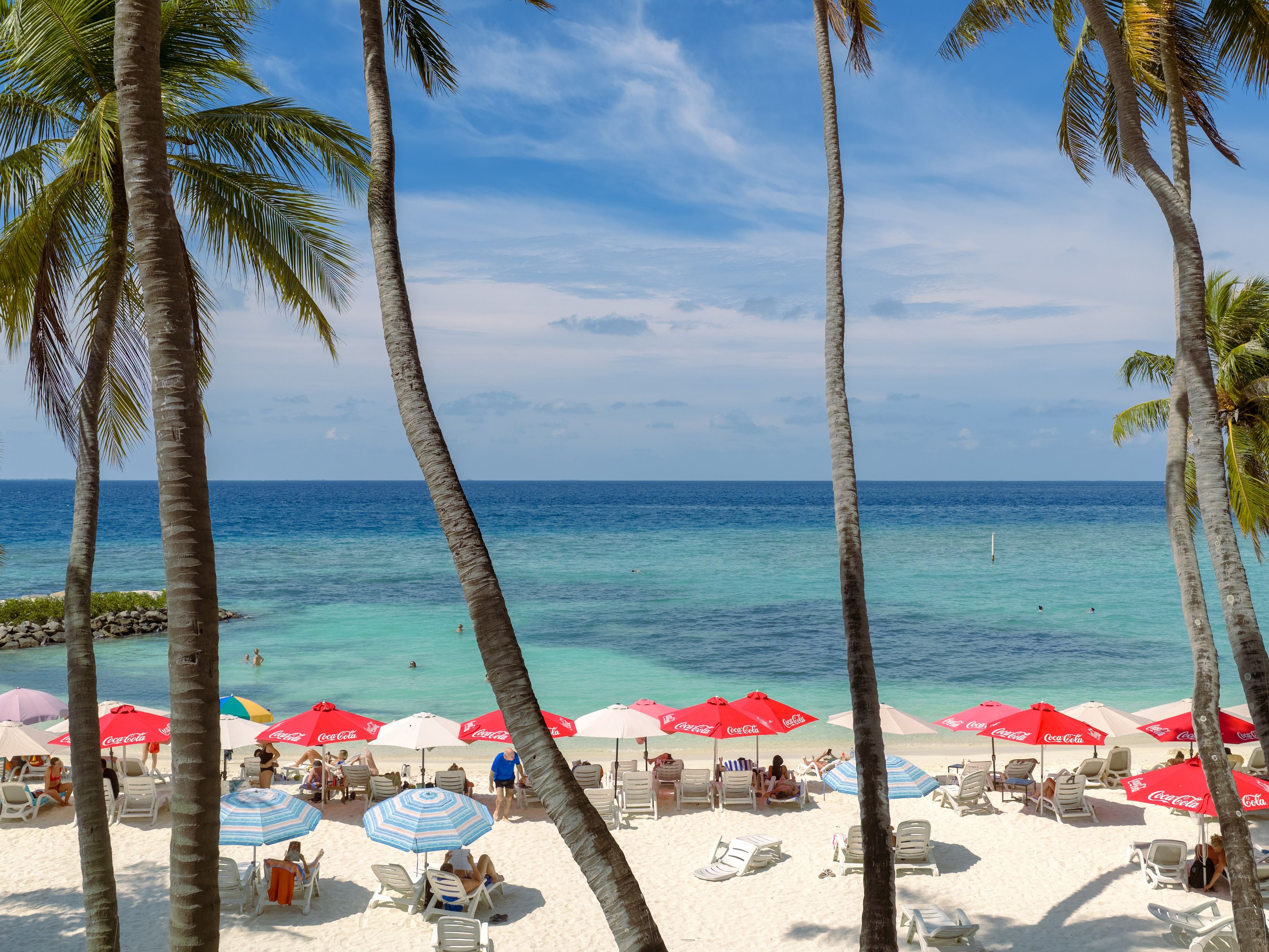 Een strand met palmbomen, helderblauw water en wit zand.