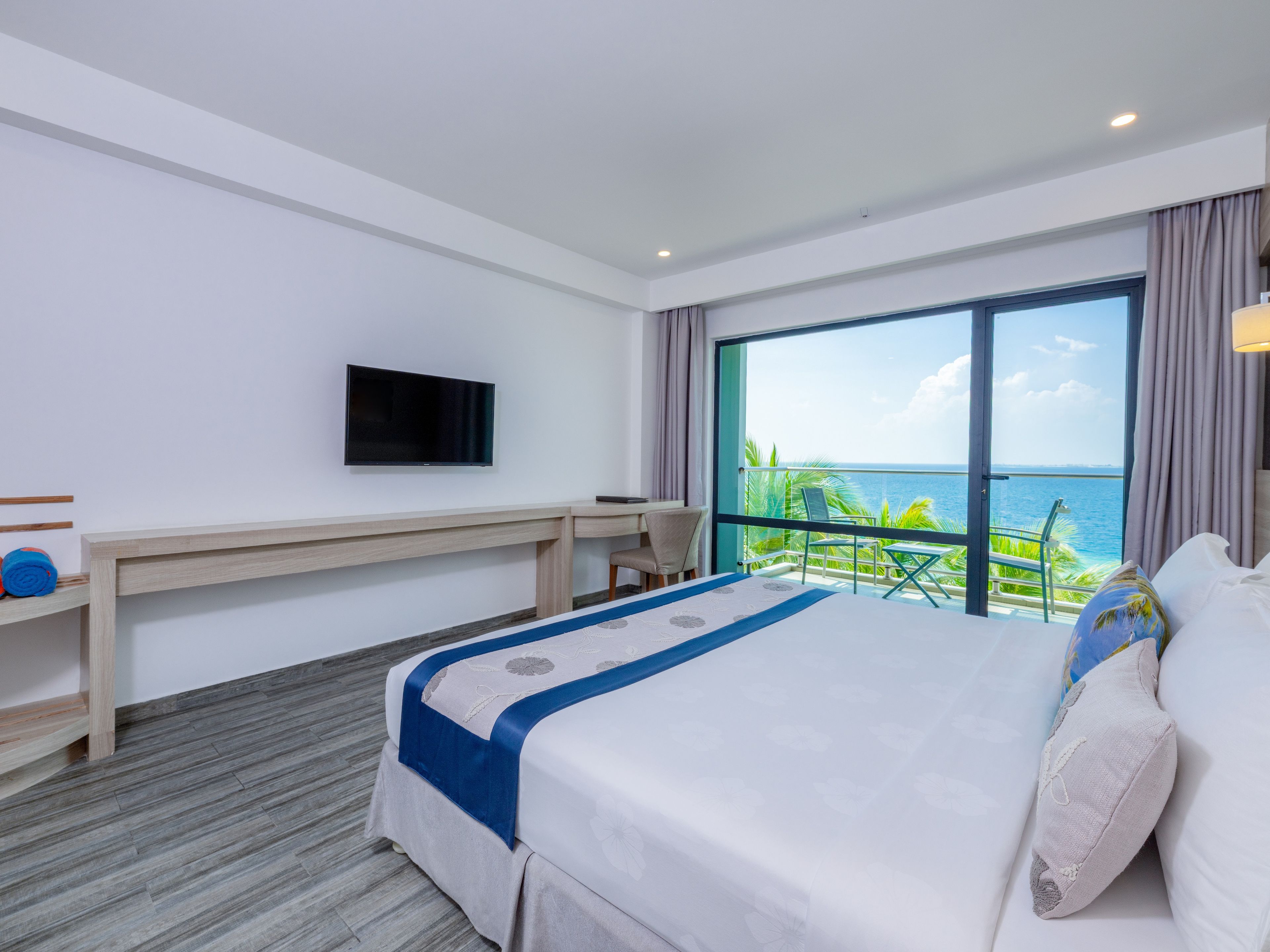 Una habitación de hotel con cama, escritorio, televisor y balcón con vista al océano.