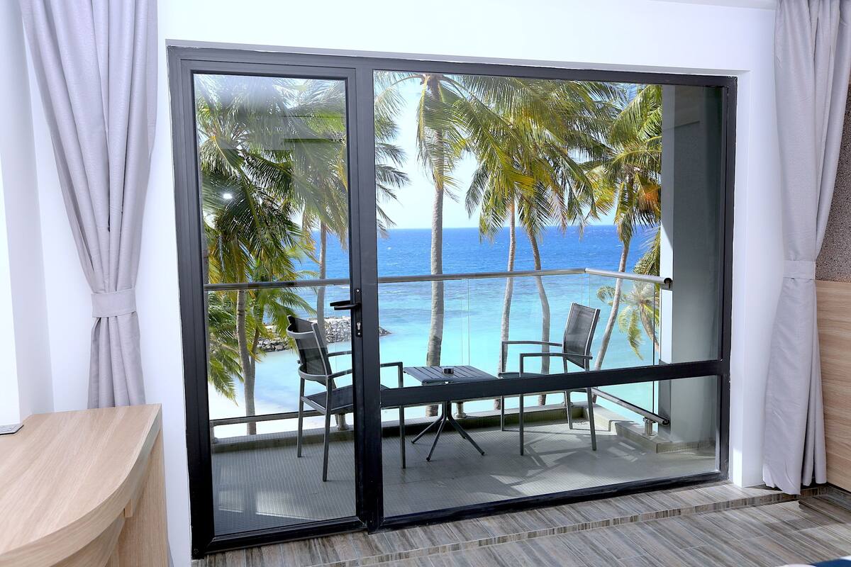 Une pièce dotée d’une porte-fenêtre coulissante donnant sur un balcon avec vue sur l’océan et les palmiers.