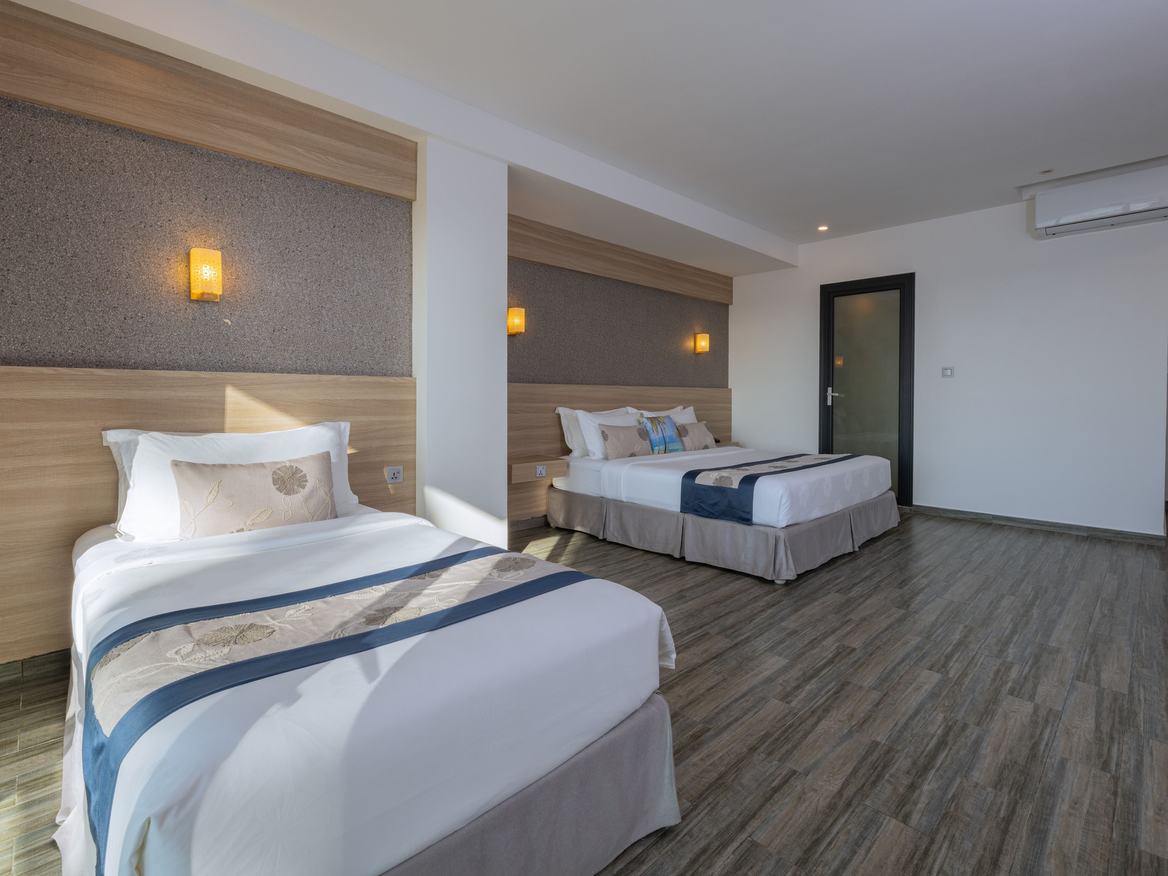 A hotel room with two beds, a wooden headboard, a wall-mounted light, and a door.