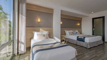 Habitación de hotel con dos camas, un ventanal con cortinas y vistas a palmeras, además de suelo de madera.