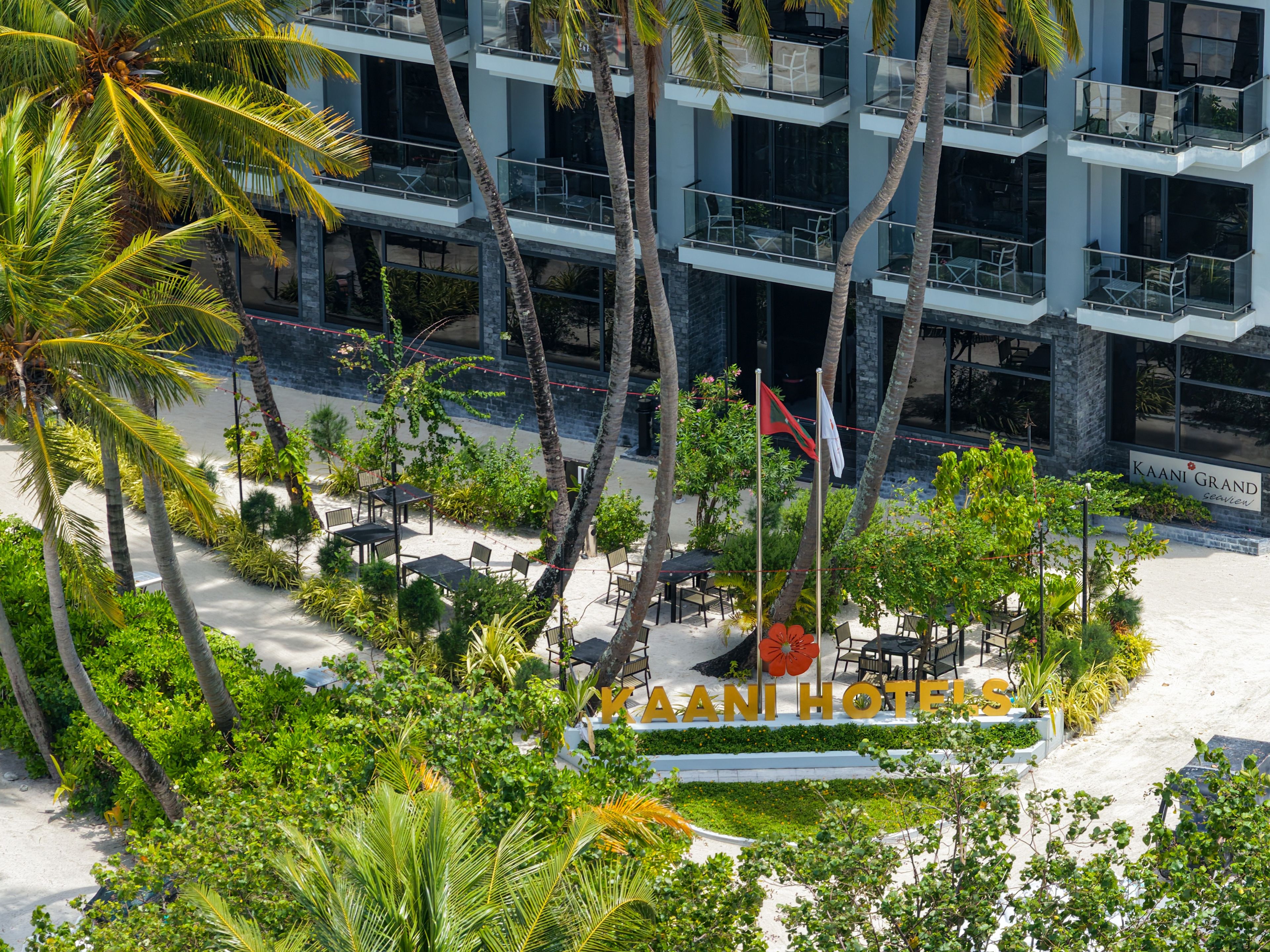 A hotel with a sign reading 'KAANI HOTELS' surrounded by lush greenery and palm trees.