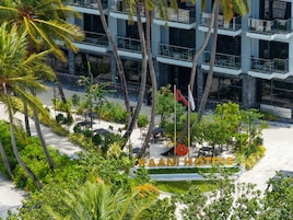 Ένα ξενοδοχείο με μια πινακίδα που γράφει «KAANI HOTELS», το οποίο περιβάλλεται από πλούσια βλάστηση και φοίνικες.