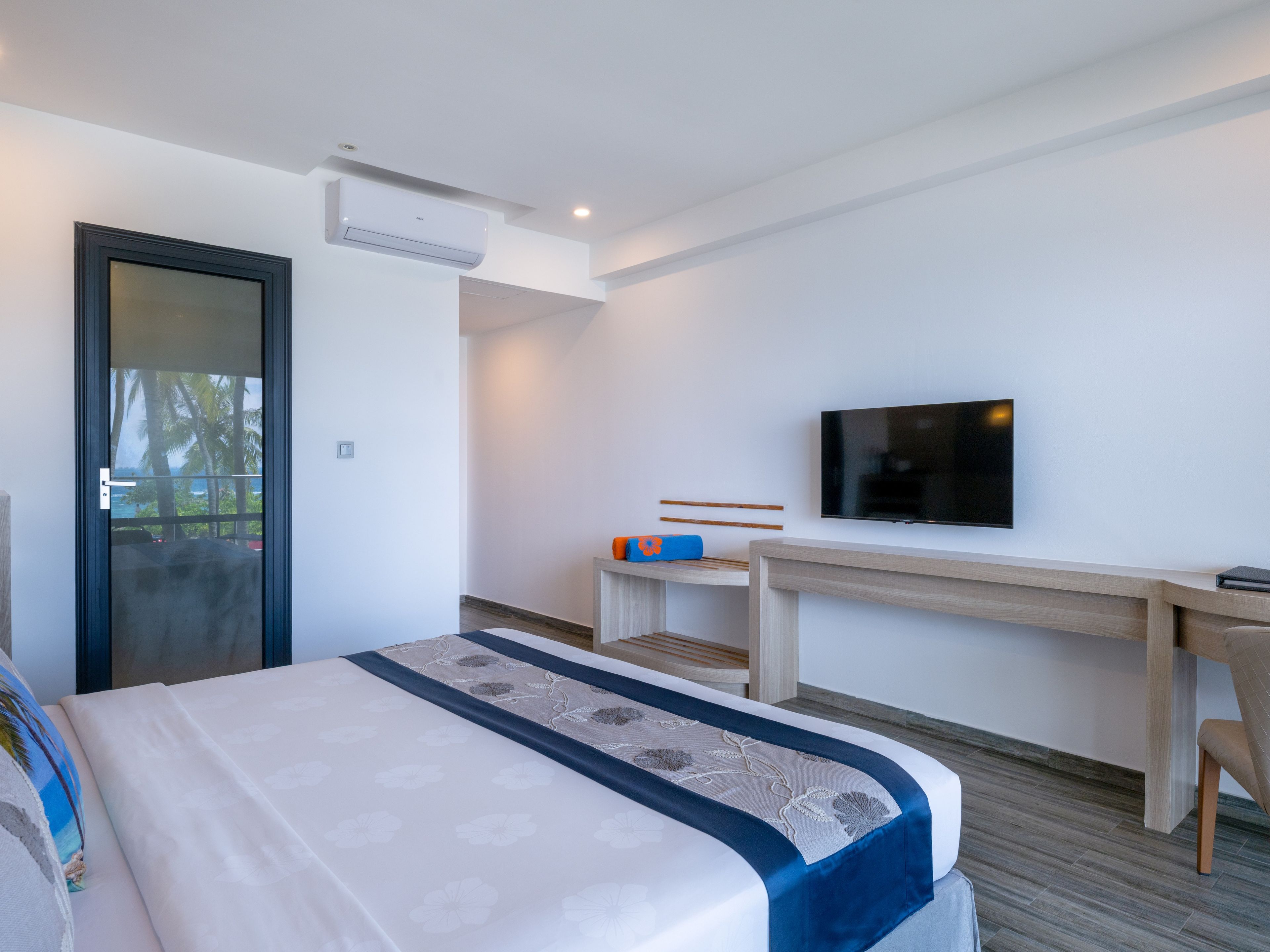 A hotel room with a bed, a desk, a television, and an air conditioning unit.