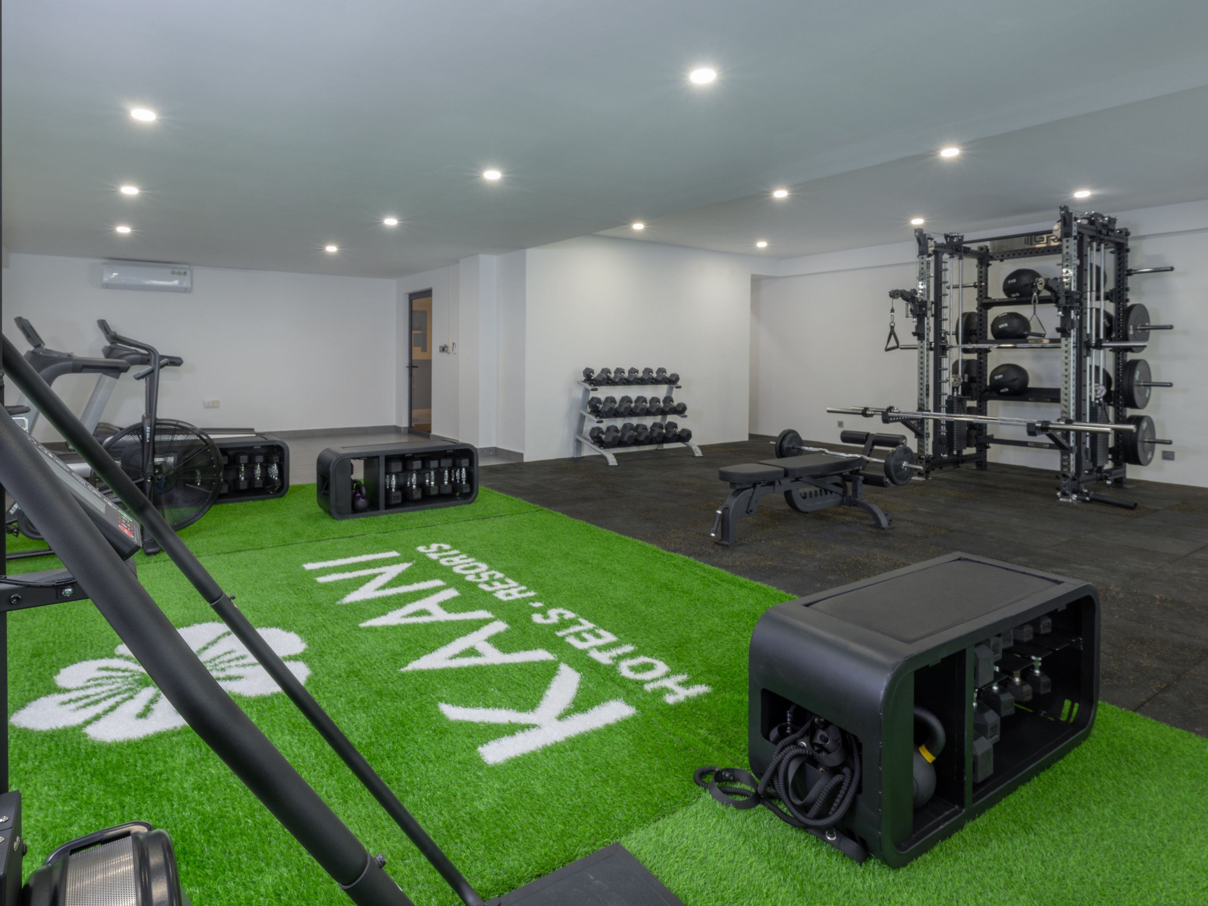 Un gimnasio con equipo de ejercicio, una zona de césped artificial verde y un soporte de mancuernas fijado a la pared.