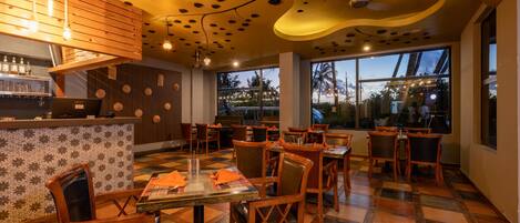 A restaurant interior with wooden furniture, a bar area, and large windows providing a view of the outside.