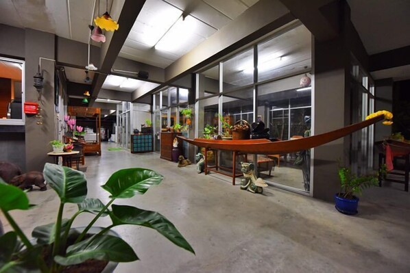 A spacious lobby with a long wooden bench, potted plants, and a large window offering a view of the street. - Namnon Place (Nonthaburi)