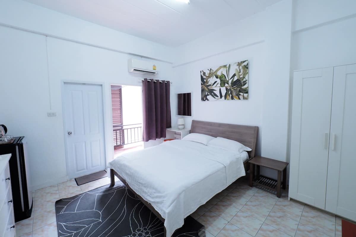 A bedroom with a bed, bedside table, wardrobe, and a window with curtains.