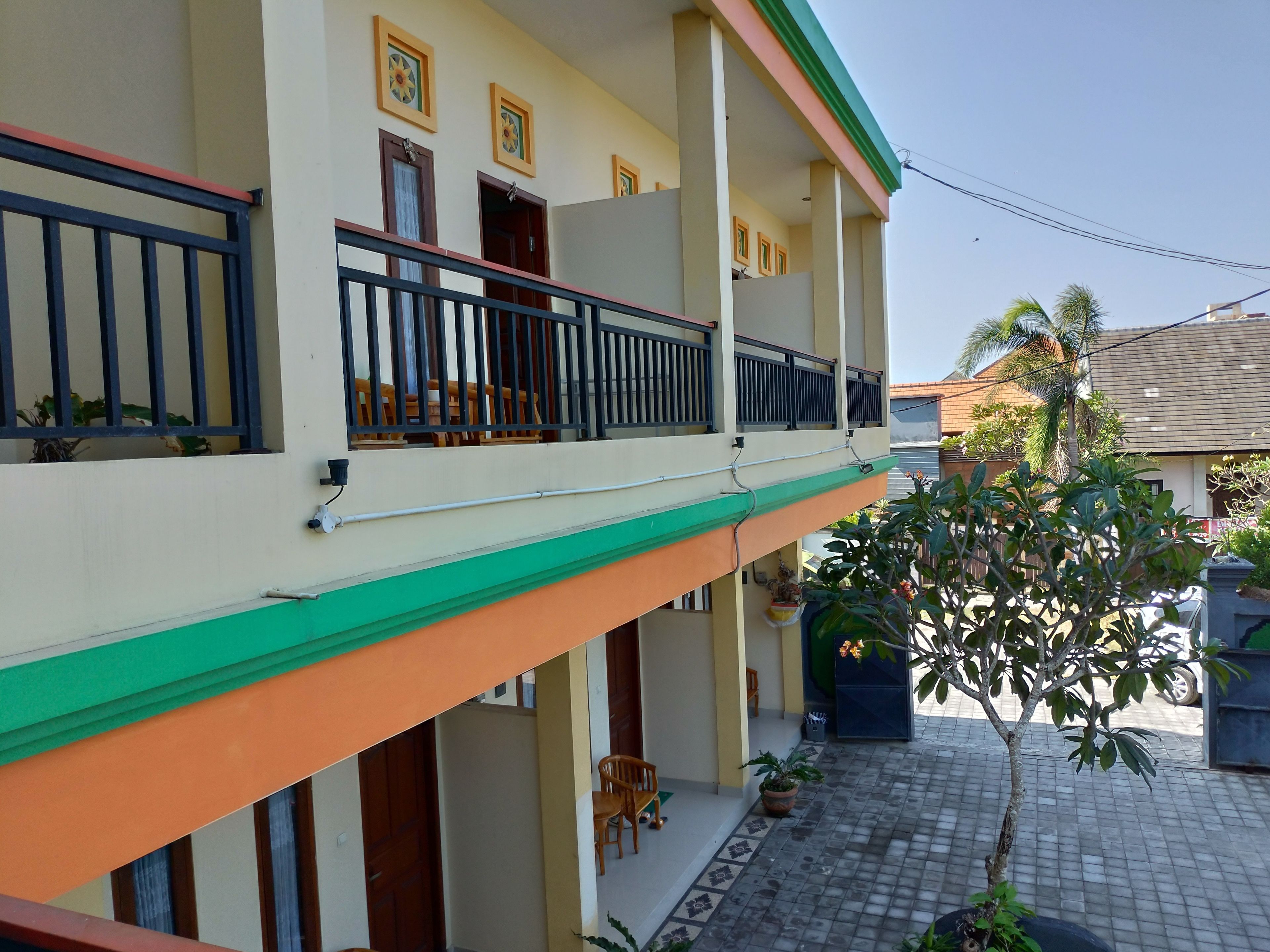 A two-story building with balconies, a tiled patio, and potted plants.