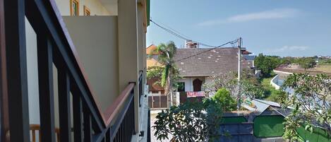 A balcony with a view of a residential area, a small tree, and parked motorcycles.