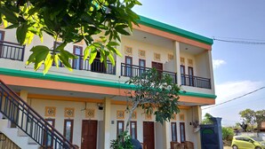 A two-story building with a staircase leading to the entrance, potted plants, and a yellow car parked outside. - Beji Ayu Homestay (Seminyak)