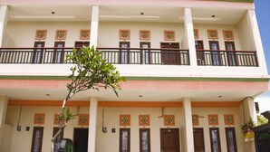 A two-story building with a balcony on the upper floor, multiple doors with flower-patterned decorations, and several potted plants in front. - Beji Ayu Homestay (Seminyak)