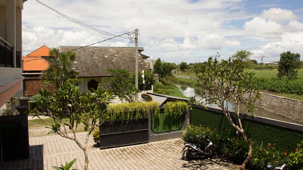 A residential area with a paved courtyard, a motorcycle, and a river in the background. - Beji Ayu Homestay (Seminyak)
