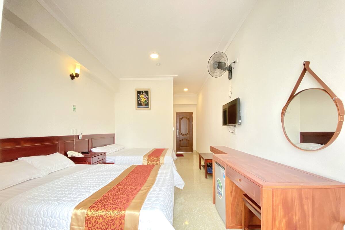 A hotel room with two beds, a desk, a mirror, a TV, and a ceiling fan.