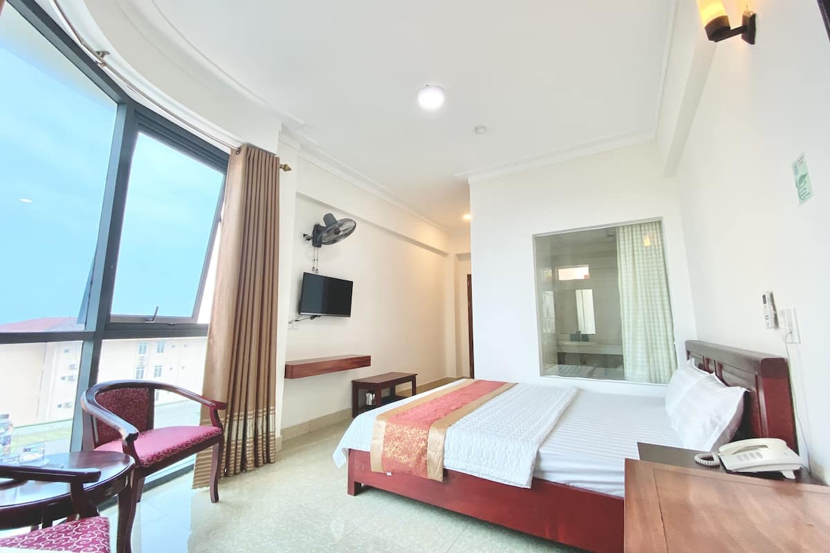 A hotel room with a bed, a desk, a chair, a TV, and a window.