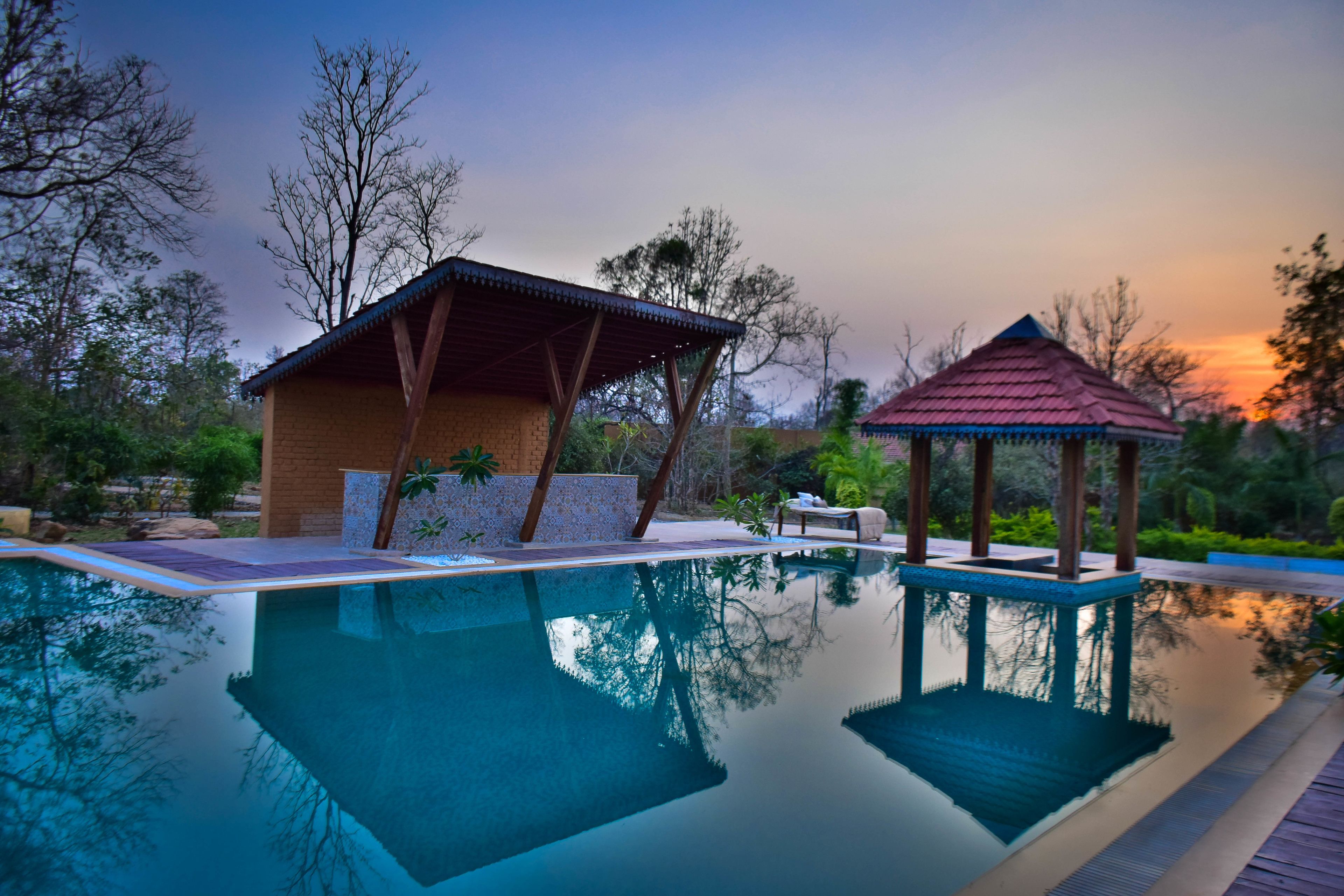 A swimming pool with a gazebo and a covered structure, surrounded by trees and greenery.
