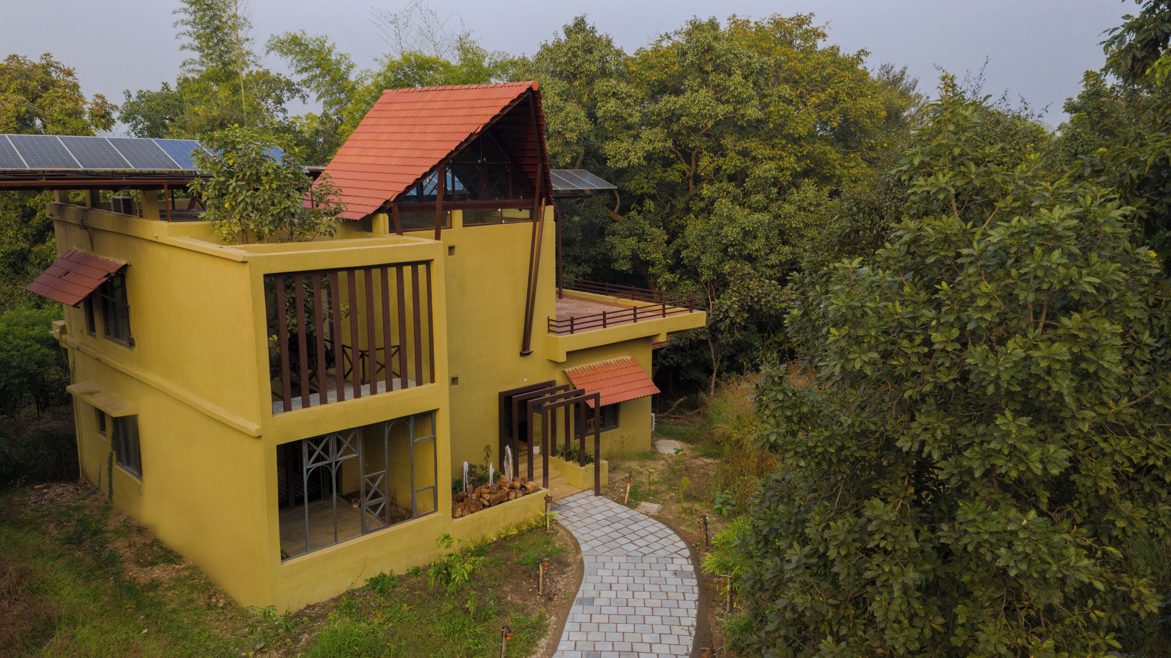 Un edificio amarillo con techo rojo, paneles solares y un camino pavimentado que conduce a la entrada.