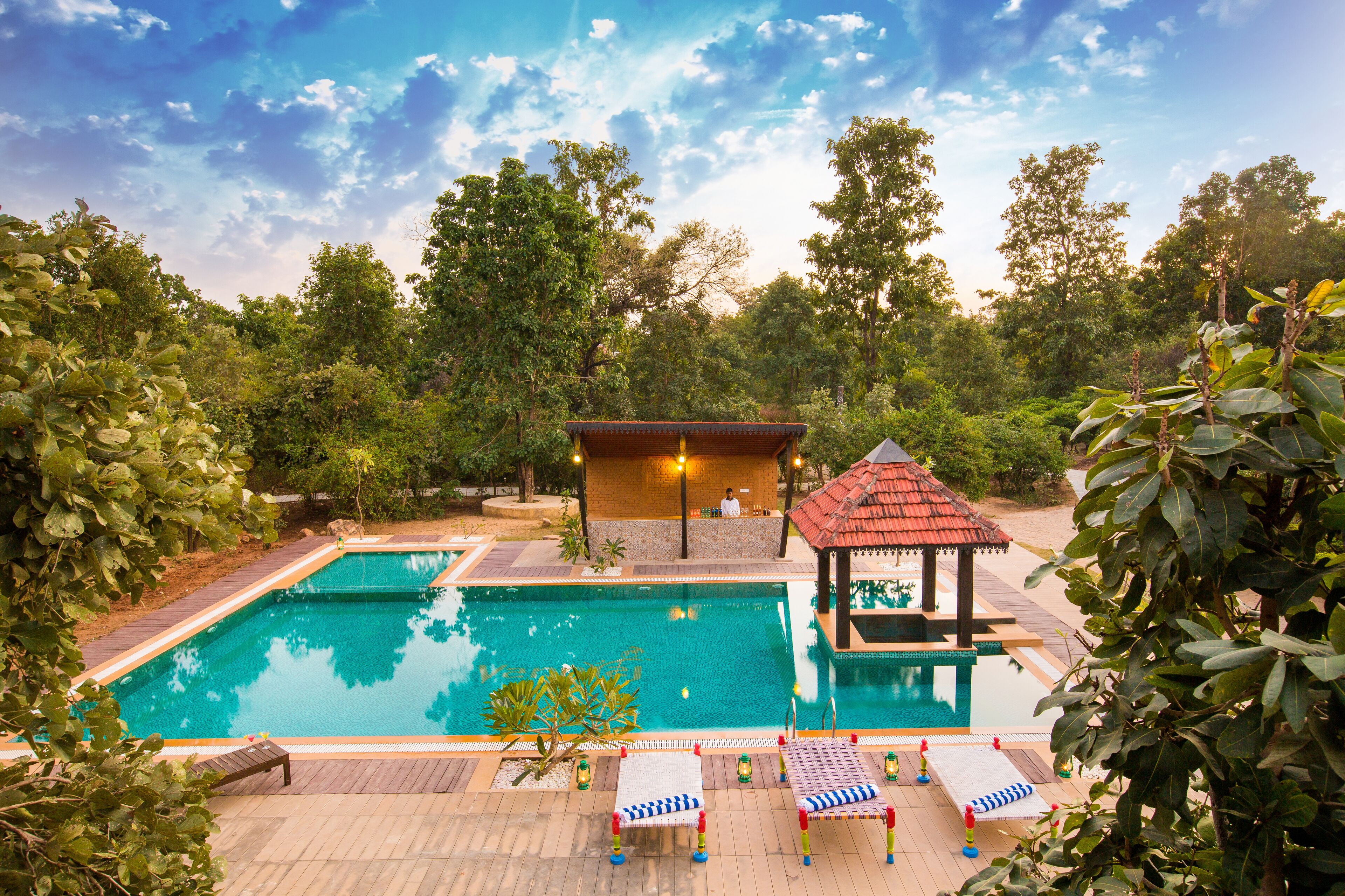 A swimming pool with two separate sections, surrounded by lush greenery and a gazebo.