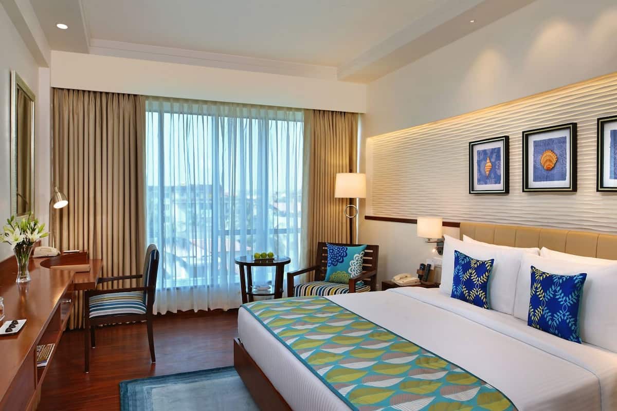 A hotel room with a bed, a desk, a chair, a TV, and a window with curtains.