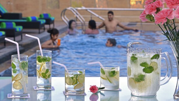 Ambiente à beira da piscina, com vista clara para a piscina, espreguiçadeiras e uma mesa com bebidas.