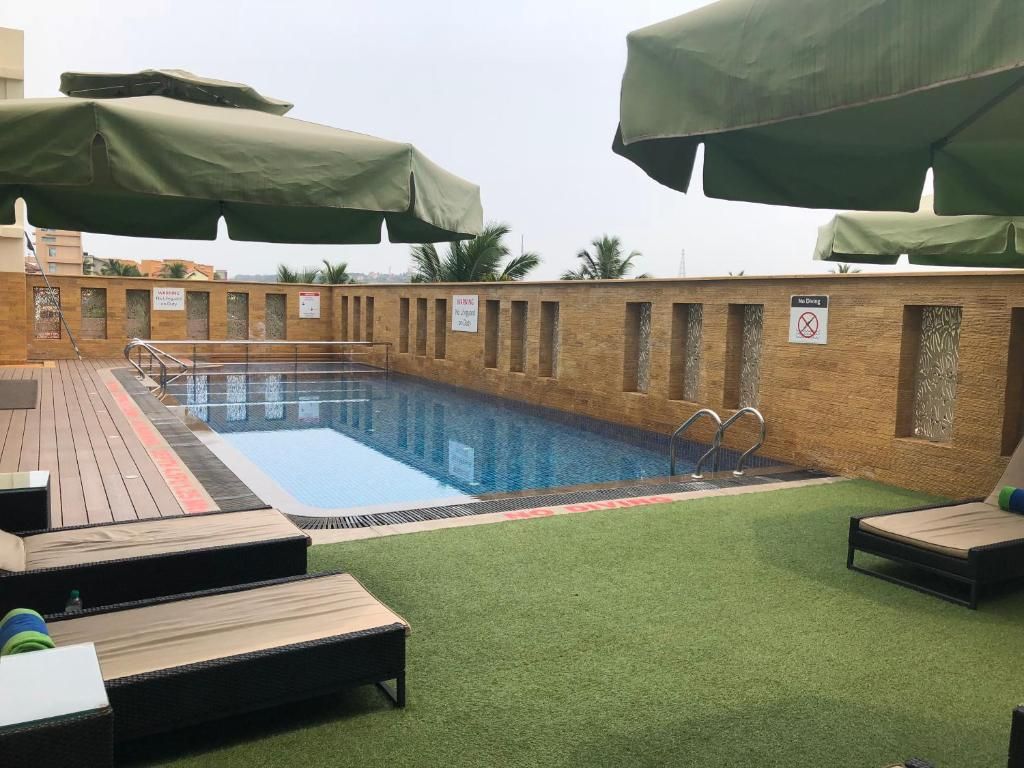 Piscina en la azotea con sillas de descanso y sombrillas, rodeada por un muro de ladrillo con un letrero de prohibición de drogas.