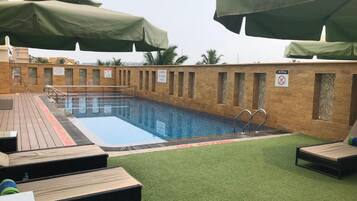 Piscina en la azotea con sillas de descanso y sombrillas, rodeada por un muro de ladrillo con un letrero de prohibición de drogas.