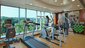 Uma academia com máquinas de cardio, esteira e um painel com tapetes de exercício.