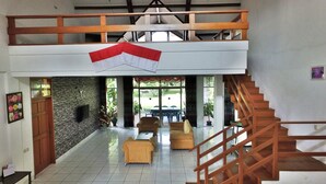 A spacious interior with a high ceiling, a staircase, and a view of the outdoors. - Vila Bunga Merah Gelatik (Lembang)