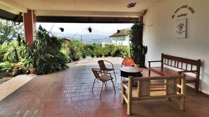 An outdoor patio with a wooden table and chairs, surrounded by potted plants and a view of the mountains. - Vila Bunga Merah Gelatik (Lembang)