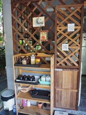 A rustic wooden structure with a sign offering free coffee and tea, a QR code, and shelves stocked with mugs and kitchenware. - Lanta Happy Hill Resort (Ko Lanta)