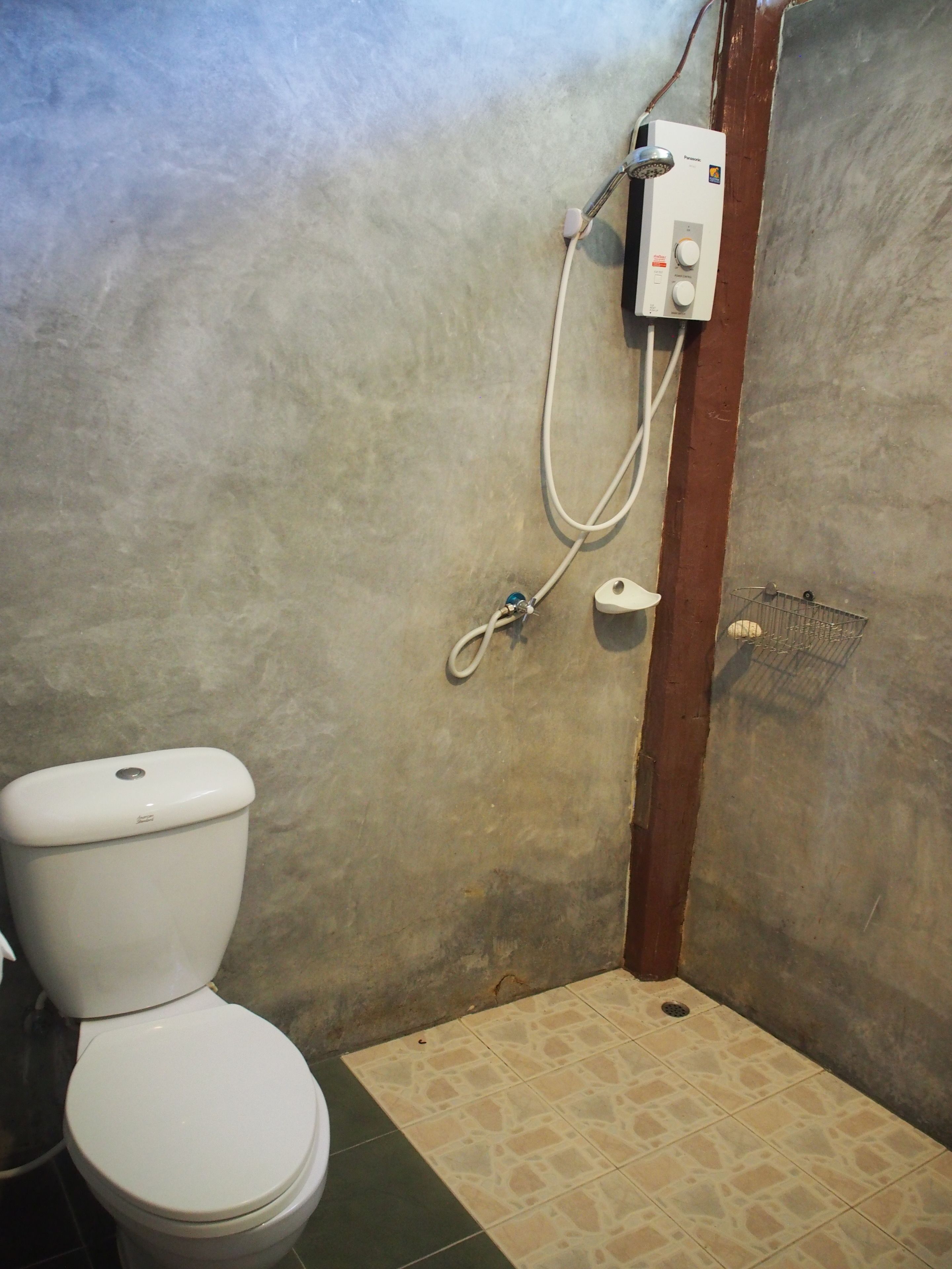 A bathroom with a toilet, a shower unit, and a tiled floor.