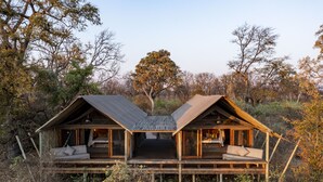 A wooden cabin with two bedrooms, each with a bed and a window. The cabin is surrounded by trees and has a wooden deck.