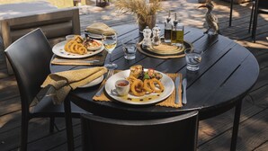 A dining table set outdoors with plates of food, glasses, and cutlery.