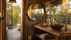 A wooden bathroom with a large mirror, a sink, and a bowl. There is a window with a view of trees.