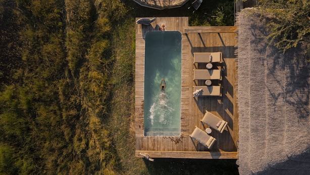 An aerial view of a wooden deck with a rectangular pool, lounge chairs, and a large umbrella.