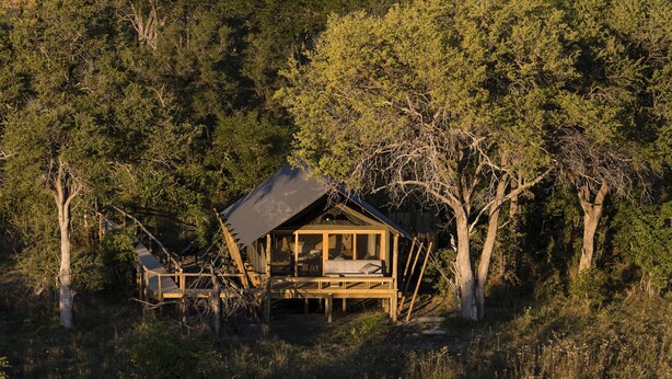 A rustic cabin with a wooden deck and a single-story structure surrounded by dense forest.