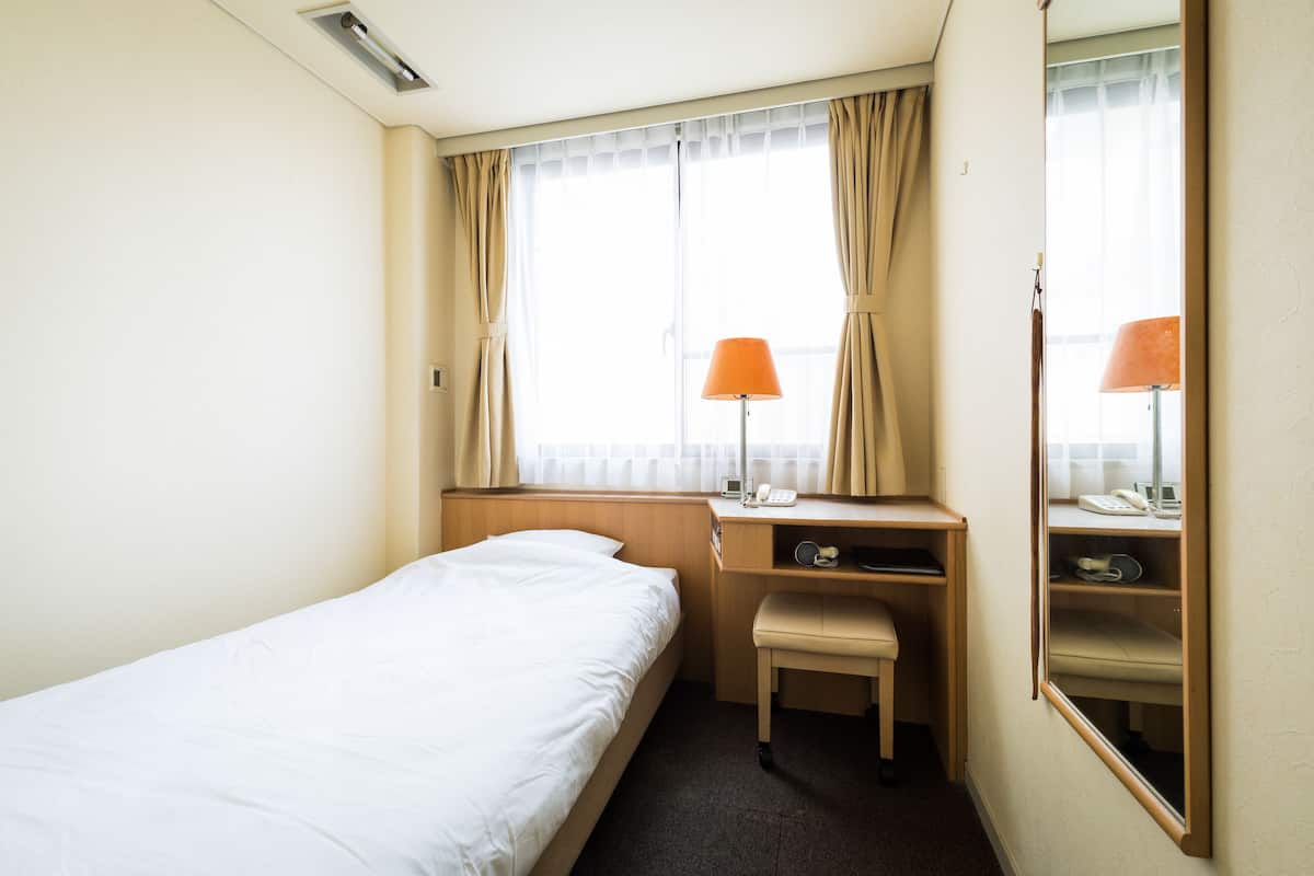 A hotel room with a single bed, a desk with a chair, a lamp, and a mirror.