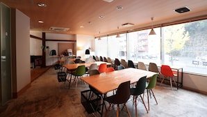 A conference room with a long table and multiple chairs, large windows with a view of the street, and ceiling vents. - Hotel Sungarden Matsuyama (Matsuyama)