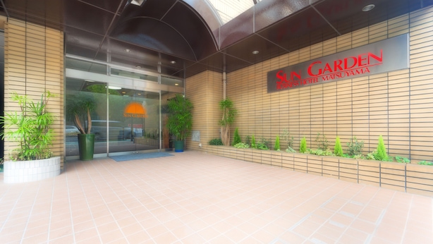 The exterior of Sun Garden Hotel Matsuyama with a modern design, including a glass entrance and a tiled walkway. - Hotel Sungarden Matsuyama (Matsuyama)