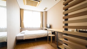 A compact hotel room with a bed, a desk, a chair, a TV, and a window with curtains. - Hotel Sungarden Matsuyama (Matsuyama)