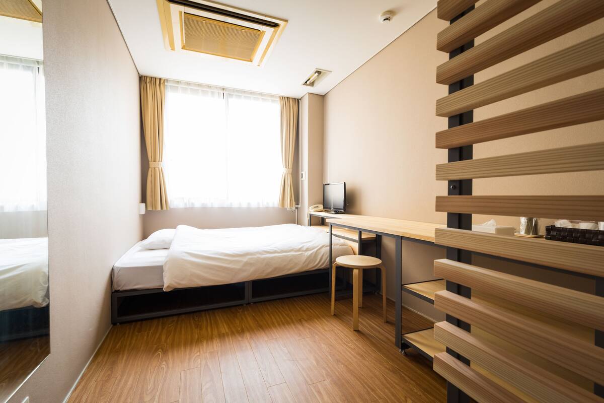 A compact hotel room with a bed, a desk, a chair, a TV, and a window with curtains.