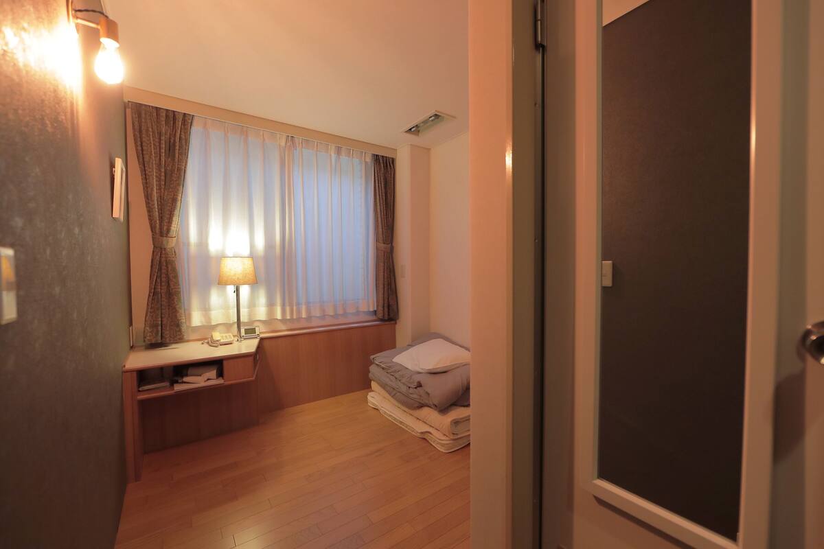 A compact bedroom with a bed, bedside table, lamp, and a window with curtains.