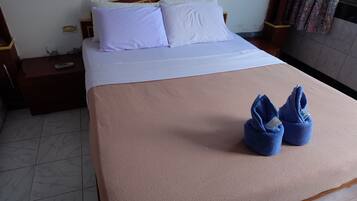 Habitación de hotel con cama, almohadas, mesita de noche, control remoto y un par de toallas sobre la cama.