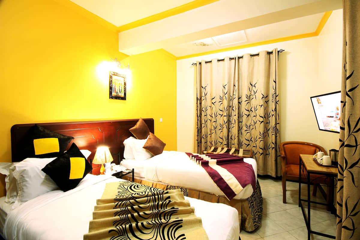 Quarto de hotel com cama, escrivaninha, cadeira, luminária e cortinas.