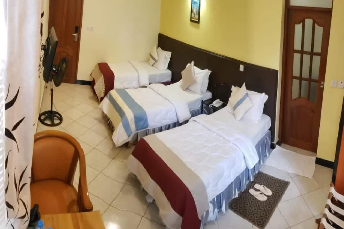 Quarto de hotel com duas camas, uma escrivaninha, uma cadeira, um ventilador e uma porta.