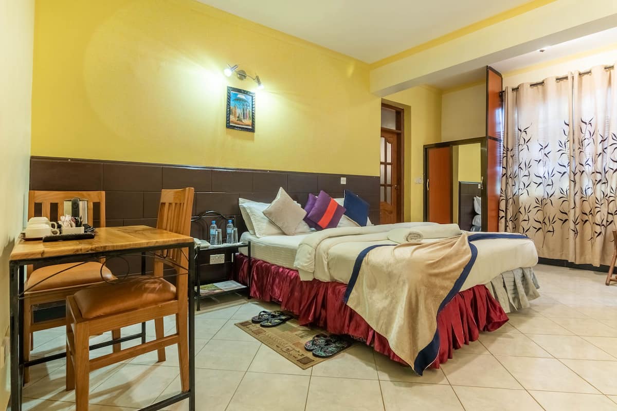 Quarto de hotel com cama, escrivaninha, cadeira e mesa de cabeceira.