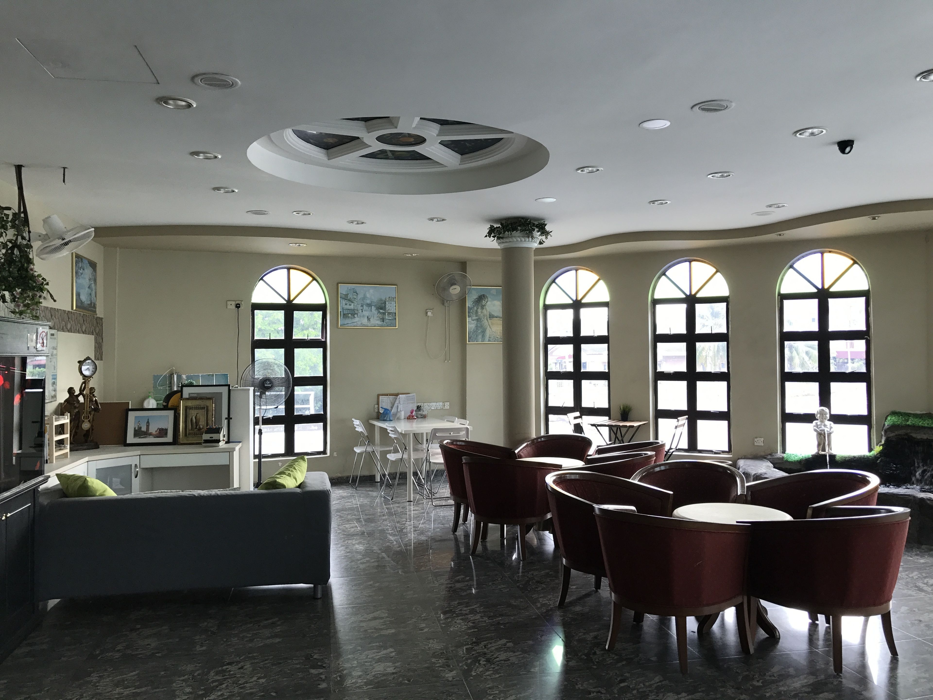 A spacious room with a high ceiling, large arched windows, and a central seating area with chairs and a table.